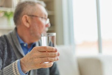Senior man holding glass drinking fresh water at home. Mature old senior thirsty grandfather takes care of his health. Healthcare water balance. Elderly healthy lifestyle