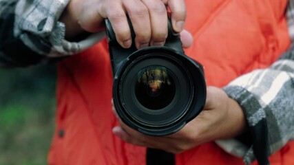Professional photographer wearing bright orange vest, carefully adjusting camera settings while standing outdoors during photo shoot