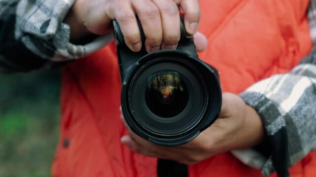Professional photographer wearing bright orange vest, carefully adjusting camera settings while standing outdoors during photo shoot