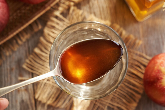Apple cider vinegar on a spoon above a glass of water