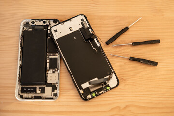 Smartphone repair process with screwdriver and disassembled mobile phone on wooden table. Tech service concept, technical support, service center, display replacement