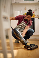Mid adult black man using vacuum cleaner at home.