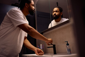 Black man looking himself in mirror in bathroom.