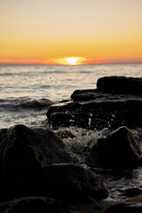 Ocean waves splash against rocks at sunset, creating water droplets