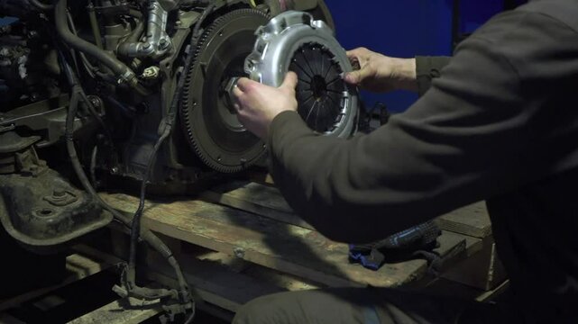 Auto mechanic installs clutch assembly. Hands expertly navigate flywheel, pressure plate, friction disc installation gearbox maintenance underway in workshop.