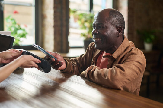 Smiling Senior Man Paying with Smartphone at Cafe Counter