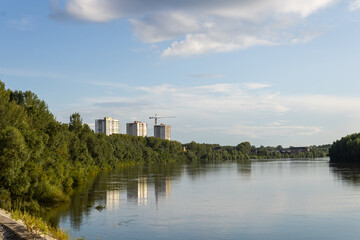 River, trees on the embankment, houses under construction and cranes. Cloudy sky on a sunny day. The capital of Bashkiria, the city of Ufa