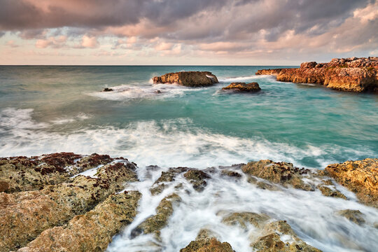 Sunrise on rocky coast with waves crashing causing water to foam.