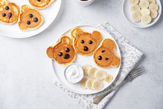 Pancakes in the form of bears with cream sauce and banana slices in a plate