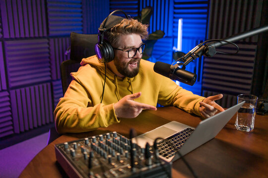 Live streaming with smiling millennial man as radio presenter with microphone, talk show or entertainment. Male person content creator and happy on podcast host in studio for recording audio or social