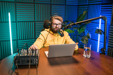 Cheerful young man recording podcast in studio. Confident man with headphones and microphone...