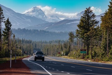 A car drives along Scenic Cascade Lakes Hwy, surrounded by lush forest and snow-capped mountains. ....