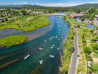 Aerial view of people tubing on the Deschutes River, enjoying a sunny day. Town and park scenery surrounds the river. Bend, Oregon, USA