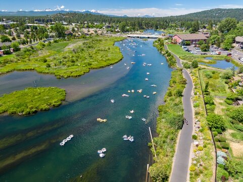 Aerial view of people tubing on the Deschutes River, enjoying a sunny day. Town and park scenery surrounds the river.  Bend, Oregon, USA