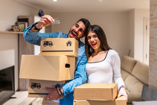 Happy couple showing keys and holding moving boxes in new home - Powered by Adobe