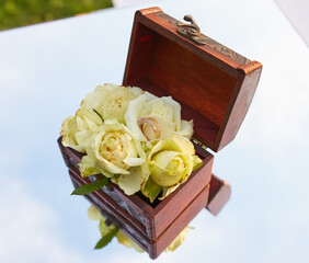 Close-Up of Wedding Rings on White Roses in Wooden Box