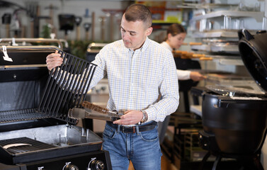Couple of young man and young woman shoppers choosing BBQ grill in hardware store