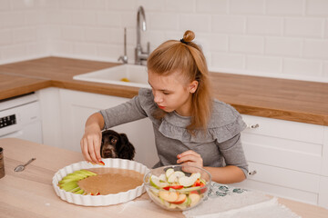 Teen girl baking in light kitchen with spaniel dog nearby asking for food