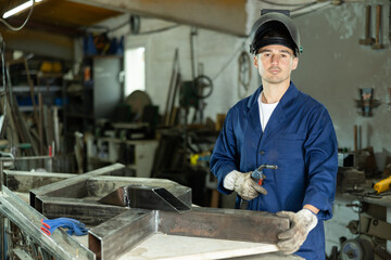 Young male welder posing with welding machine in workshop