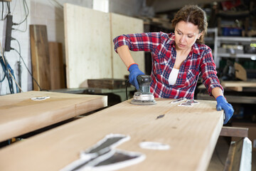 Woman sanding a wooden board using a sanding machine