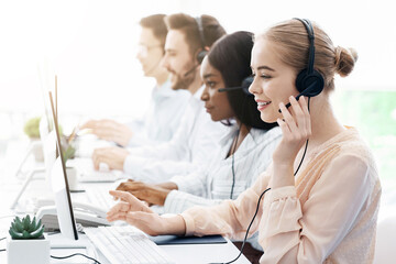 Team of helpline operators with headsets consulting clients at call center office, blank space