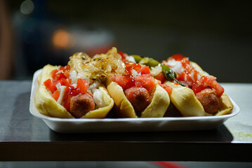 Close-up of several hot dogs loaded with toppings of diced tomatoes, onions, and ketchup on buns