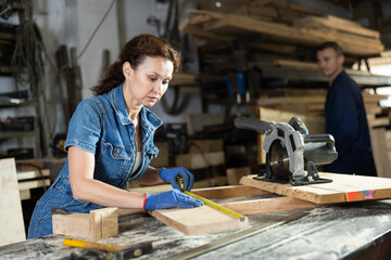 Work in woodworking enterprise - woman measures length of wooden board with a tape measure