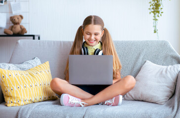 Online Chat. Frontal portrait of cheerful girl sitting with laptop in lotus position on couch with...
