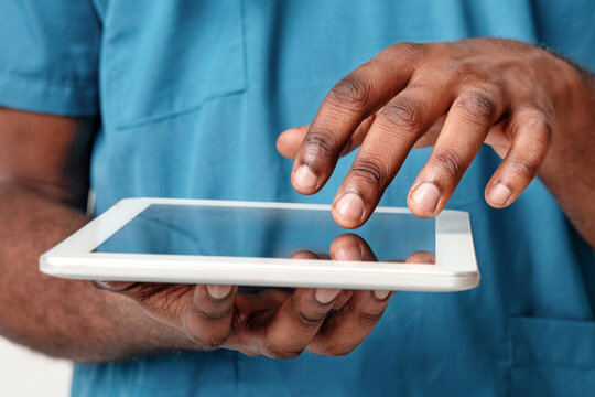 A young African American doctor is focused on a tablet, likely retrieving patient data or medical resources. The modern healthcare setting emphasizes the integration of technology in medical practice.