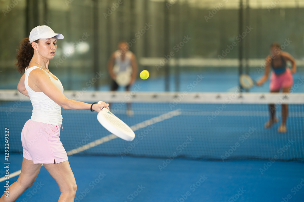 Wall mural Adult female tennis player playing against young woman and man on tennis court