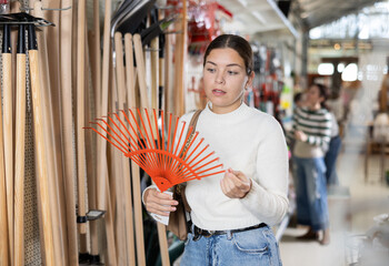 Young woman with interest chooses rake in a hardware store for gardening