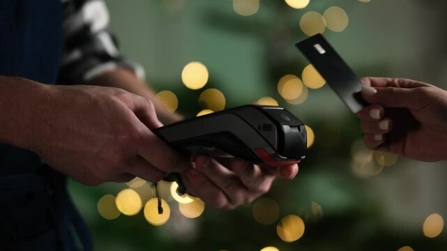 Female Hand Pays By Card On A Pos Terminal Against A Blurred Christmas Background