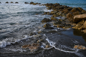 Obraz premium Waves gently lap against rocky shore at sunset with vibrant colors and serene atmosphere