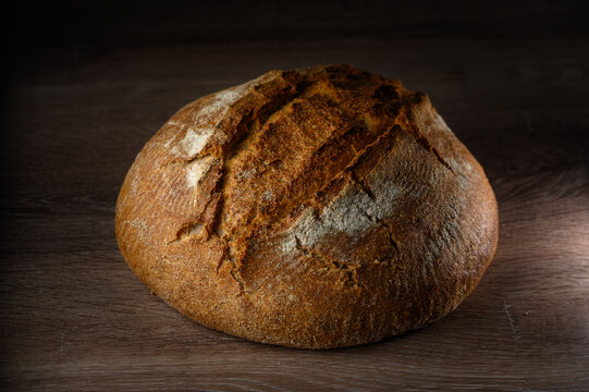 Artisan bread loaf resting on wooden surface with warm light highlighting crust details