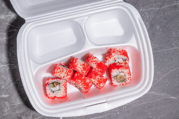 A styrofoam container with vibrant sushi rolls coated in bright red tobiko, featuring a seafood and vegetable filling.