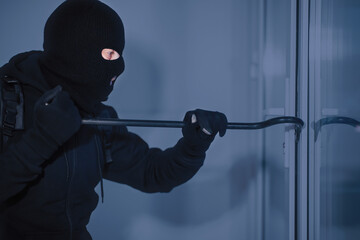 Intrusion Concept. Side view portrait of disguised prowler breaking house or office door with...