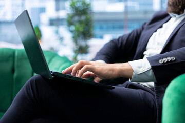 Motivated young leader working in a luxurious urban workspace, reviewing financial forecasts and tracking sales performance. Chief executive officer browses laptop in his office. Close up.