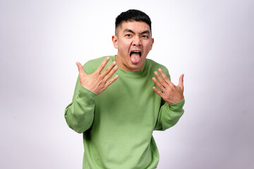 An Asian man in a green sweatshirt makes a disgusted and exaggerated expression, sticking out his...