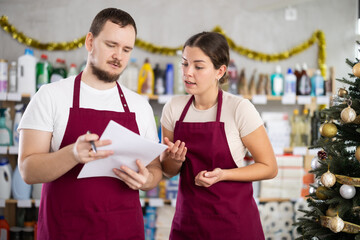 Young man and woman sellers conducting inventory in household chemicals store decorated for...