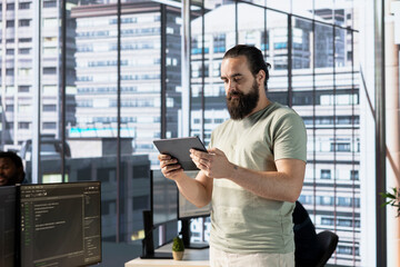 Programmer creating machine learning models that can process and analyze data to improve and automate decision making processes, looking at tablet. Man programming in office using device
