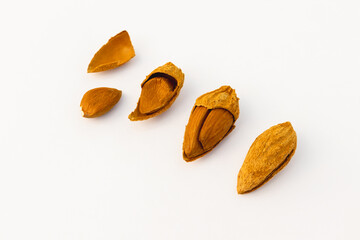 A close-up of almonds in various stages of being cracked open, showing the shells and nuts inside, placed on a white background.