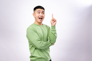 An excited Asian man in a green sweatshirt raises his index finger with an open-mouthed expression,...