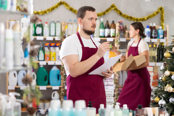 Male salesperson keeps track of goods while female salesperson stocks shelves in a supermarket before Christmas