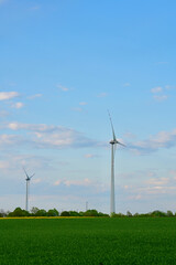 In the open spaces of a green agricultural field, two wind power generators