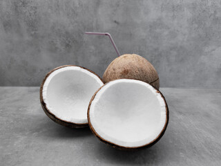 Fresh coconut halves with whole coconut and straw on gray background. Copy space, banner