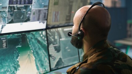 Fototapeta premium Army specialist working in war room operating surveillance tech, evaluating target data. Close up on dispatcher doing job in HQ base of operations, engaging enemy forces, camera A