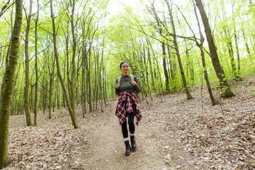 Obraz premium Happy female hiker walking along a winding path through a lush green forest, breathing in the fresh air and soaking in the beauty of nature during an invigorating hike