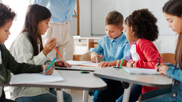 Group of preteen children studying with teacher in classroom at elementary school, having group project and discussing tasks. Teamwork concept