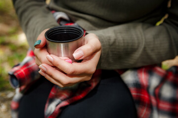 Naklejka premium Female hiker is warming her hands with a hot beverage in a metal cup during a trekking trip in the forest, enjoying a moment of peace and rest