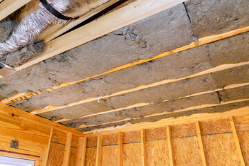 Installing insulation between exposed beams in wooden structure for improved energy efficiency during construction new house